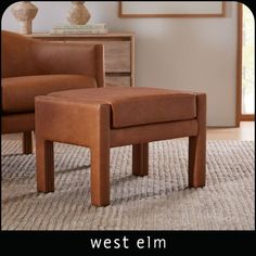 a brown foot stool sitting on top of a rug next to a chair and table