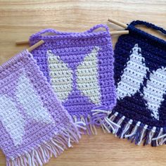 two crocheted bags are sitting next to each other on a wooden surface with knitting needles