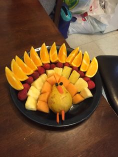 a black plate topped with fruit and a turkey shaped like an orange on top of it