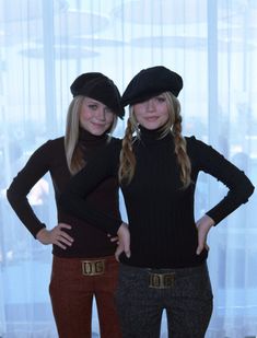 two young women standing next to each other in front of a window wearing black hats