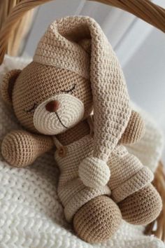 a crocheted teddy bear sitting on top of a white blanket next to a wicker basket