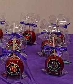 there are many candy apples wrapped in cellophane and tied with purple ribbon on the table