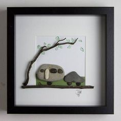 two rocks sitting on top of a tree branch in front of a white wall with a black frame