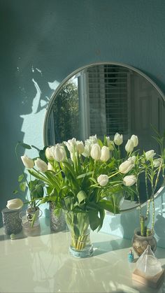 a vase with white flowers sitting on a table in front of a mirror and other items