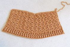 a crocheted piece of cloth hanging from a hook on a white surface,