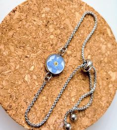 Beautiful stainless steel chain and bezel holding an original handmade resin forget me not charm. The charm contains a hand dried and pressed forget me not flower set on a white background to enhance its natural  colours and beauty. Hard wearing stainless steel 23cm Adjustable Slider Bracelet Extender Chain with Ball Ends.  Forget-me-nots symbolize true love and respect. When you give someone these tiny blooms, it represents a promise that you will always remember them and will keep them in your thoughts. They are also considered a symbol of fidelity and faithfulness. ... Please Note: there may be variations in colours due to lighting and subtle variations in the flower itself if more than one in stock. please keep away from moisture and direct sunlight to maintain the piece to its best. Bracelet Extender, Forget Me Not Flower, Slider Bracelet, Natural Colours, Wedding Jewelry Bracelets, Flower Bracelet, Forget Me Not, Sympathy Gifts, Wedding Bracelet