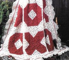 a red and white crocheted blanket sitting on top of a wooden table next to a christmas tree