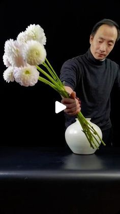 a man is arranging flowers in a vase on a black table with a dark background