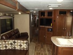 the interior of an rv with wood flooring and brown leather couches, cabinets, and sink