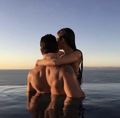 two people sitting on the back of a swimming pool with their arms around each other