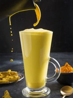 a cup filled with yellow liquid next to spoons and orange powder on a table