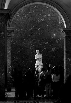 a black and white photo of a woman standing in the middle of a room surrounded by people