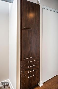 a tall wooden cabinet in the corner of a room with white walls and wood floors