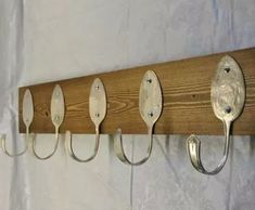 five spoons are hanging from a wooden rack with hooks on the wall behind them