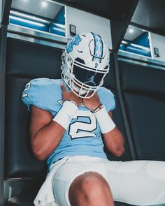 a football player sitting in the locker room with his head resting on his hands while wearing a helmet