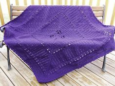 a purple crocheted blanket sitting on top of a wooden bench next to a fence