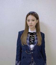 a woman in a blue jacket and plaid skirt standing next to a wall with her hands on her hips