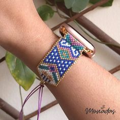 a woman's arm with a beaded bracelet on it and a plant in the background