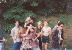 a group of young people standing next to each other in front of trees and bushes