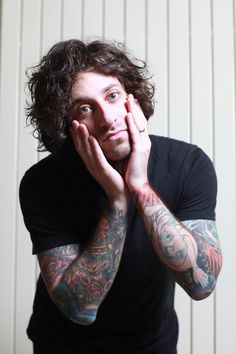 a man with tattoos on his arms and chest posing for the camera while holding his hands to his face