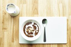 a white plate topped with a bowl of food next to a cup of coffee on top of a wooden table