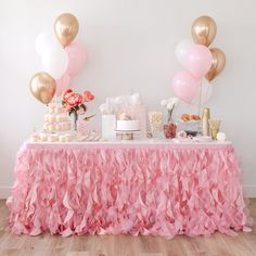 a table topped with lots of pink and gold balloons next to a cake on top of a wooden floor