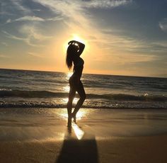 a woman standing on top of a sandy beach next to the ocean at sunset or dawn