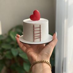 a hand holding a small white cake with a red heart on top and a ladder painted on the side