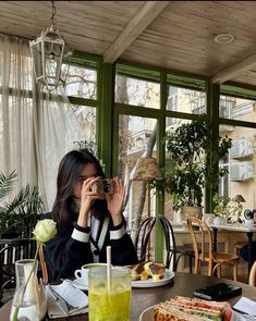 a woman sitting at a table with food and drinks in front of her taking a photo