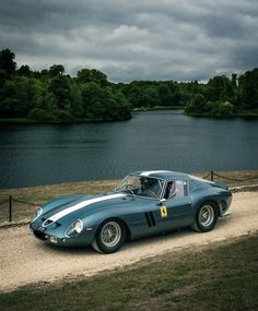 a blue sports car parked on the side of a road next to a body of water