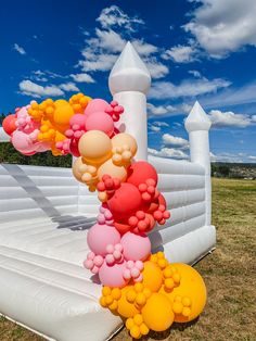 an inflatable arch with balloons attached to it on the grass next to a white fence