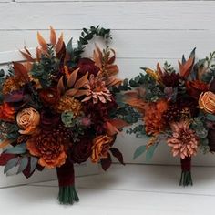 two bridal bouquets with orange and red flowers are on display against a white wall