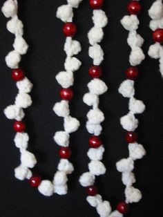 a crocheted beaded necklace with red beads and white flowers on black background