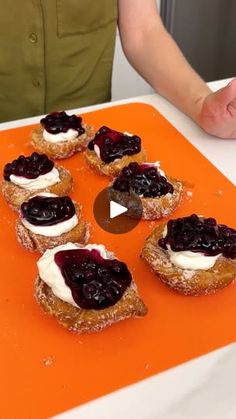 the person is making small pastries on the orange cutting board with white icing