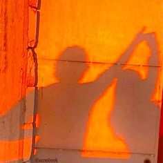 the shadow of a man holding a baseball bat in front of an orange wall with graffiti on it