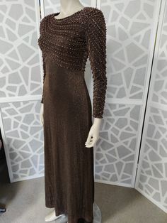 This late  1960s dress is so beautifully beaded with pinky brown pearls and bronze beads in a diagonal pattern on the bodice and they continue down the sleeves to wrist length. You would be sure to get lots of compliments wearing this stunning dress The label is Vie Victoria Royal of Hong Kong from the 60s. The bronze lurex dress has a high neckline, fitted bodice and waist then skims the hips to an A line skirt to ankle length The dress has a back nylon zipper, has small shoulder pads to help w Fitted Beaded Maxi Dress For Evening, Beaded Fitted Maxi Dress For Evening, Elegant Brown Maxi Dress For Evening, Brown Floor-length Maxi Dress For Evening, Elegant Embellished Brown Dresses, Fitted Brown Embellished Dress, Party Floor-length Brown Dress, Brown Fitted Evening Dress, Fitted Brown Evening Dress For Party