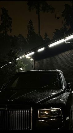 a black rolls royce parked in front of a building at night with its lights on