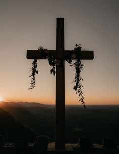 a wooden cross with flowers on it at the top of a hill in front of a sunset