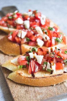 two pieces of bread with tomatoes and cheese on them, sitting on a cutting board