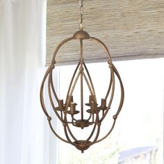 a chandelier hanging from the ceiling in front of a window with white curtains