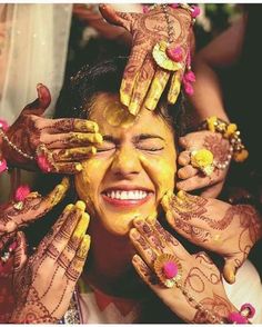 a woman with henna on her face and hands covered in yellow paint smiles for the camera