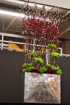 a vase filled with red flowers sitting on top of a table next to a black wall