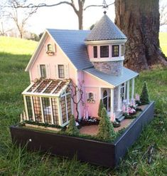 a pink doll house sitting on top of a wooden box in the grass next to a tree