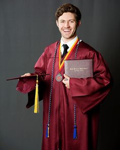 a man in a red graduation gown holding his diploma and smiling at the camera while standing against a black background