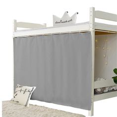 a white bunk bed with a curtain over it's headboard and pillows on the floor