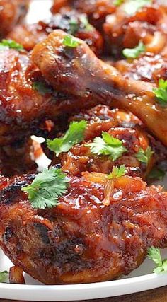 chicken wings covered in sauce and parsley on a white plate with a wooden table