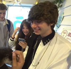 two boys and one girl are looking at a cell phone while the boy is holding a monkey