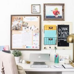 a white desk topped with a laptop computer sitting next to a wall covered in pictures