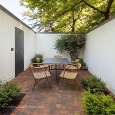 an outdoor dining area with table and chairs, surrounded by greenery on either side