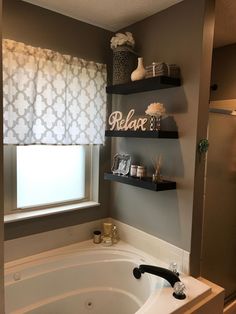 a bath tub sitting under a window next to a shelf filled with candles and other items